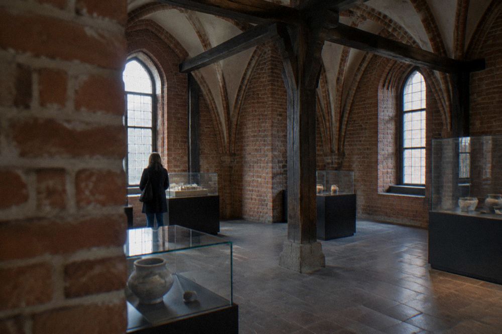 A museum ticket counter in a Gothic brick interior with a visitor buying a paper ticket