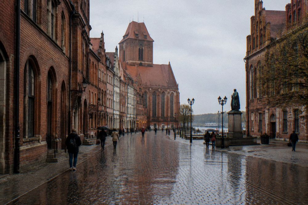 A narrow medieval street in Toruń with wet cobblestones reflecting the brick facades after rain
