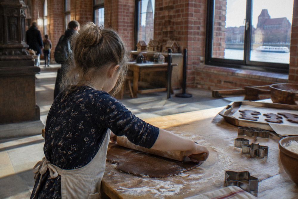 A child rolling gingerbread dough on a wooden table during a baking workshop