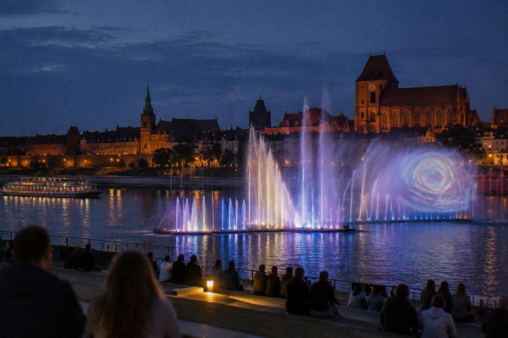 Water and light show playing at an outdoor multimedia fountain in the evening