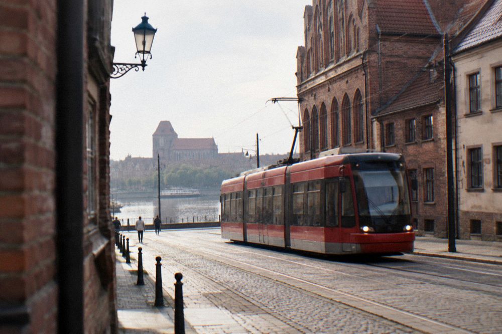 A red city tram passing historic buildings on a Toruń street
