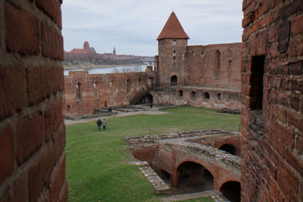 Red brick ruins of the Teutonic castle in Toruń with grassy courtyard and arched cellars open to the sky